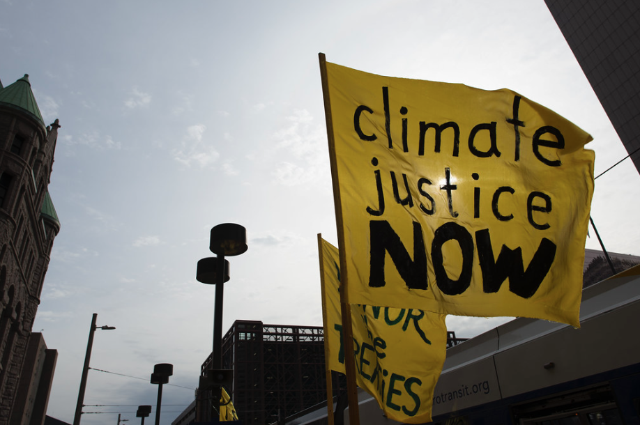 Yellow flag at protest that has the words, climate justice now written on it